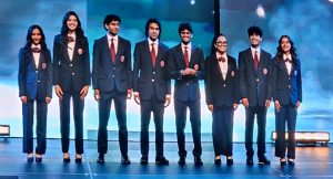 A line of eight students stand on a stage wearing suits, smiling at the camera.