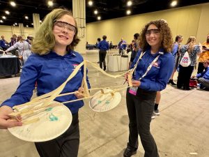Two female students stand near each other with a handmade device, smiling at the camera.
