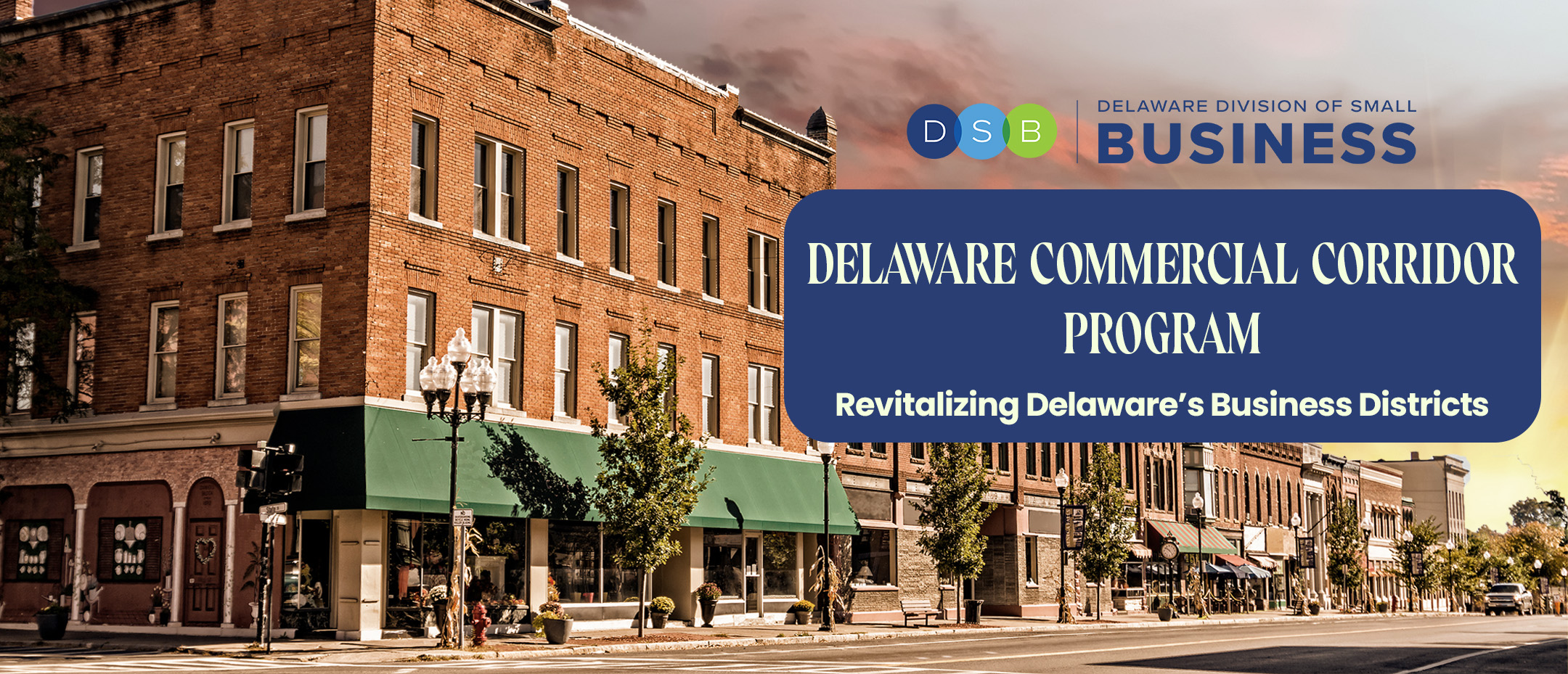 Several store fronts shown, lining a street that make it look like a downtown area from a diagonal view. The DSB logo sits near the top of the right third of the photo. A navy blue block with white lettering sits below it. The text reads Delaware Commercial Corridor Program. Subtext reads Revitalizing Delaware's Business Districts