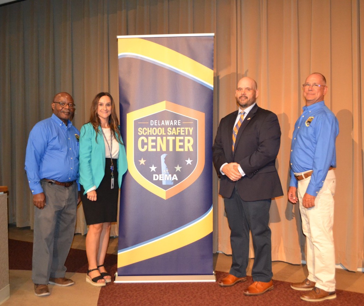 Members of the Delaware School Safety Center and Department of Education stand beside a Delaware School Safety Center banner in a conference room.