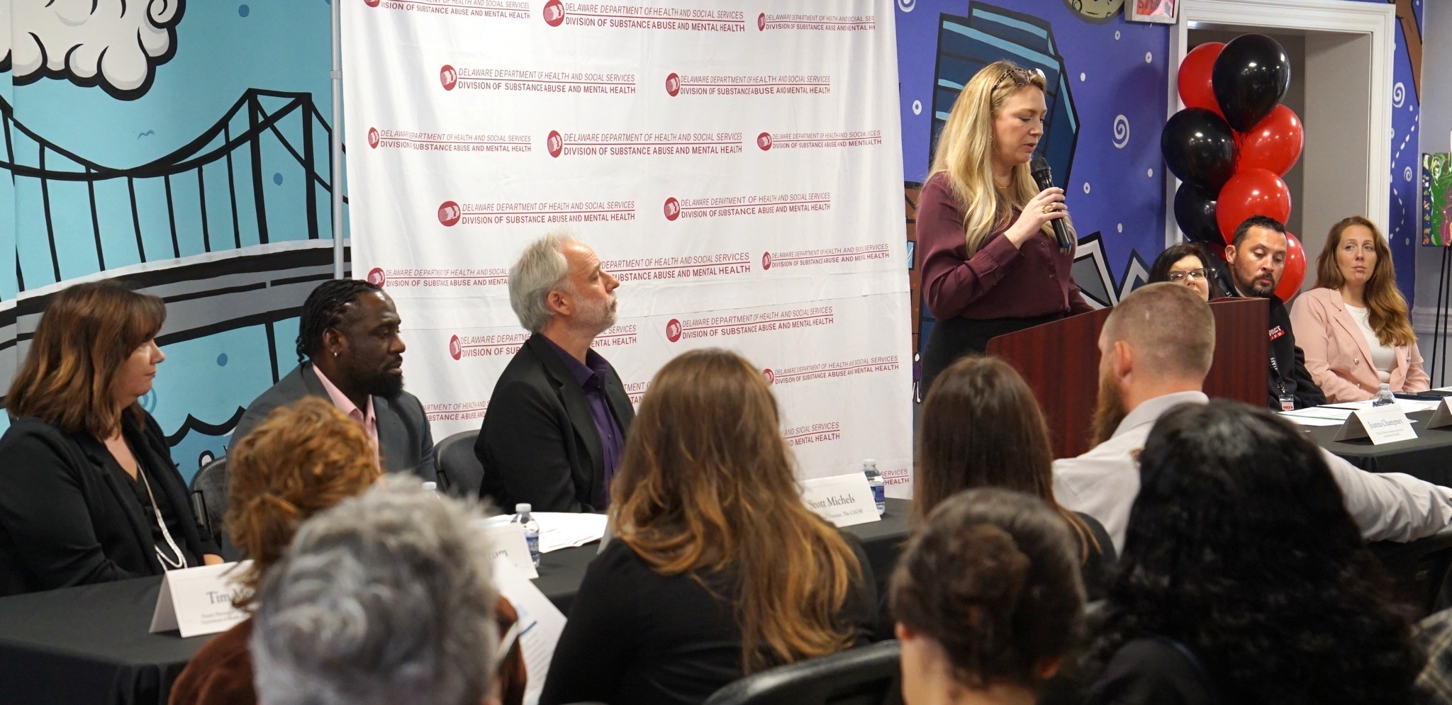 Woman stands at brown podium in front of a crowd.